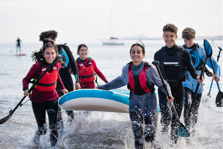 kids running through the water on the beach, holding up an inflatable boat. Yacht & Boat Safety Requirements in Australia.